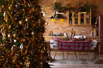 Close up Christmas tree with lights garland in modern dining room with served table with dishes, festive decorated empty apartment house for New Year family celebration, winter holiday concept