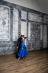 Fototapeta na wymiar young man dancing with a girl in a blue ballroom dress in a gray dance hall