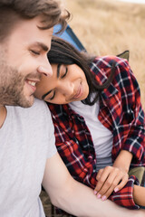 Smiling african american woman sitting near boyfriend on burred foreground during trip