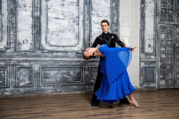 young man dancing with a girl in a blue ballroom dress in a gray dance hall