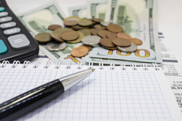 close-up of a Notepad with a pen on a blurry background of dollars with coins and a calculator