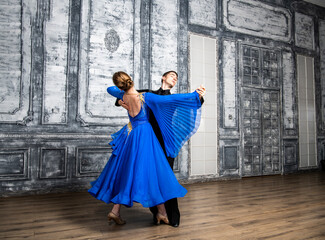 Fototapeta na wymiar young man dancing with a girl in a blue ballroom dress in a gray dance hall