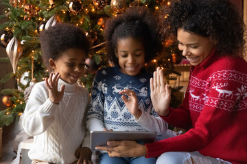 Close up happy African American family making video call to relatives on Christmas, sitting near festive tree at home, smiling mother with two kids using tablet, chatting online, waving hands - Powered by Adobe