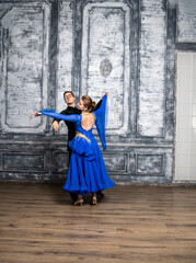 young man dancing with a girl in a blue ballroom dress in a gray dance hall