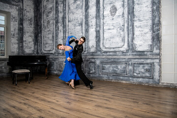 young man dancing with a girl in a blue ballroom dress in a gray dance hall