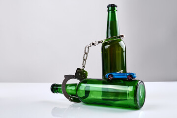 Arrest of drink drive concept. Green glass bottles with handcuffs and miniature blue car.