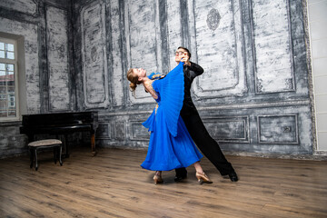 Naklejka premium young man dancing with a girl in a blue ballroom dress in a gray dance hall