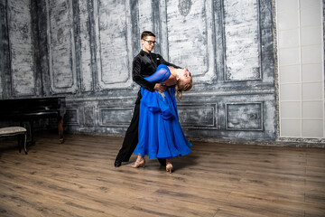 Fototapeta premium young man dancing with a girl in a blue ballroom dress in a gray dance hall