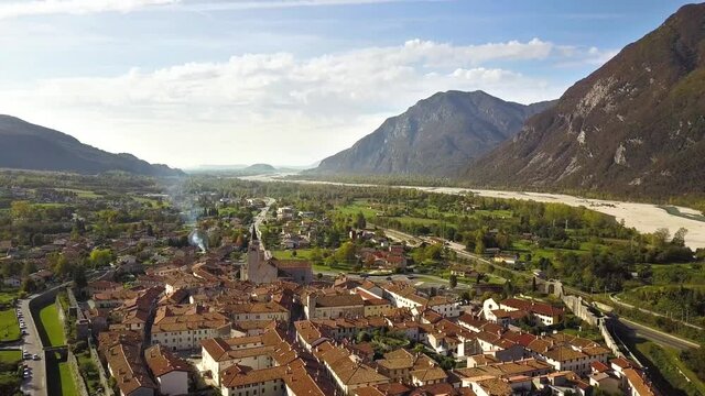 Aerial view of a small historic town Venzone in Northern Italy with red tiled roofs of old buildings and majestic Alps mountains.