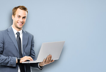 Portrait image of happy smiling confident businessman working with laptop, against grey color background. Success in business concept studio picture. IT professional specialist man.
