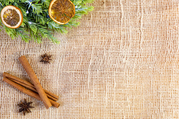 Fototapeta na wymiar close-up of cinnamon stick, anise, green wreath with lights and dry oranges, bright natural and vintage christmas decoration on jute background, raw ingredients, flat lay