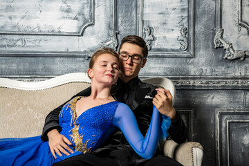 young couple in evening dresses sitting on a white couch in the dance hall