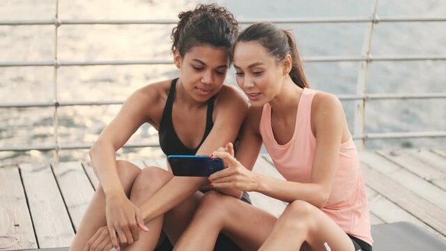 Young positive happy fitness women using mobile phone outdoors at the beach together