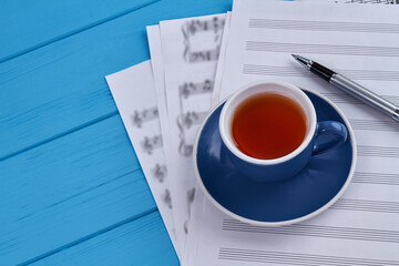 Cup of tea and songwrite papers. Pen and blue wood.