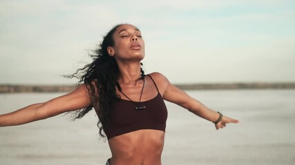A good looking african american woman wearing sportswear is doing sport exercises standing outside at the beach - Powered by Adobe