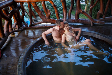 Happy romantic couple taking a bath in a jacuzzi, outdoors on a romantic vacation on a blurred background of nature at a summer resort. Outdoor Jacuzzi.