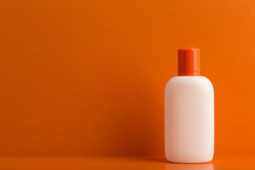 Sunscreen lotion in unbranded white jar on orange background with space for text