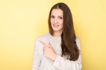 Happy attractive tatar brunette girl smiling toothy and pointing with finger at blank space for product or text isolated on yellow background