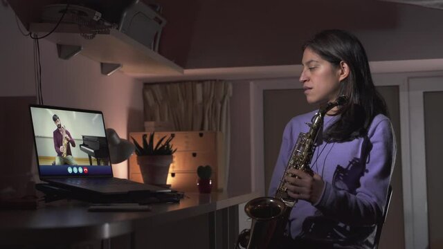 Young Woman is learning a musical instrument online. Video call with saxophone teacher. Remote learning from home  Online education in times of Coronavirus