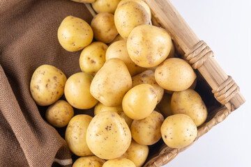 New raw potatoes in a wicker basket on a brown background close up, flat lay, top view