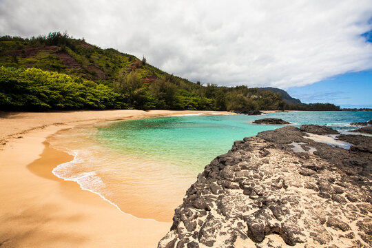 Laval rocks and headland on a Hawaiian coastline and a sweeping sandy beach.