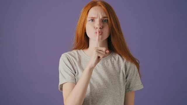 A serious young woman is doing silence gesture standing isolated over a violet background