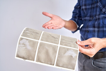 Home air conditioner replacement and cleaning concept. Professional fixer shows dirty filters close...