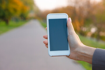 Smartphone in female hand  on autumn  background,with copy space.