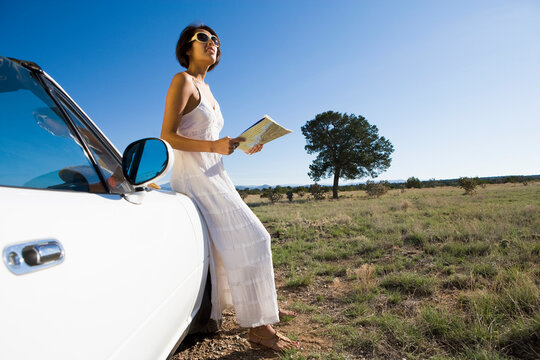 Native American woman by a convertible sports car on desert dirt road holding a map