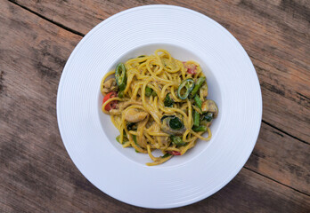 Top view Green curry spaghetti with chicken in a white plate placed on a wooden table.