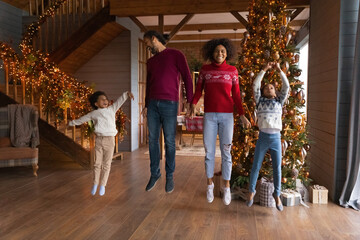 Fototapeta na wymiar Overjoyed African American family jumping near Christmas tree, enjoying winter holidays at home, happy mother and father with son and daughter having fun, laughing and dancing, flying in air
