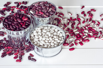 white and red beans in metal bowls on a wooden background close-up. background with white and colored beans.