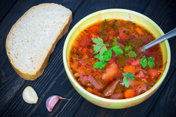 Borscht with parsley in plate on vintage table with garlic and bread. Ukrainian national dish