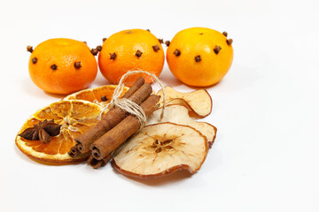 Mandarynki ozdobione goździkami, suszone pomarańcze, jabłka i laski cynamonu na białym tle

