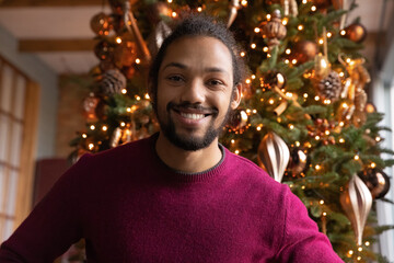 Head shot portrait smiling African American man chatting online with Christmas tree on background, making video call to relatives or friends, using webcam, blogger recording vlog for social network