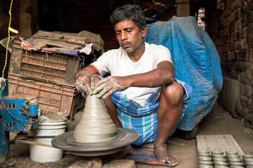 Indian potter making small pot or Diya for Diwali with clay on potters wheel in his small factory. Manufacturing traditional handicraft with clay.