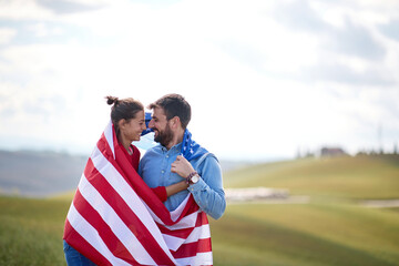 A couple in love in romantic moments cloaked by American flag at the meadow. Election, campaign, freedom concept