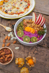 Purple smoothie bowl with fresh kiwi, Almond, banana, pumpkin seeds, apple and Pizza cheese on a wooden table