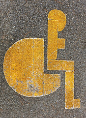 Weathered yellow handicap disability parking symbol on asphalt.