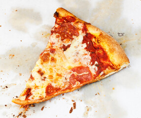 Slice of pepperoni pizza on greasy wax paper.