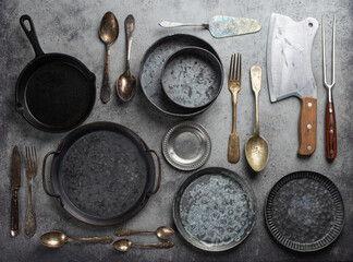 Old vintage tableware and kitchen utensils on rustic stone background, top view. Various metallic plates, bowls, cast-iron pan, cutlery. Set of assorted antique dish ware, kitchen and cooking concept