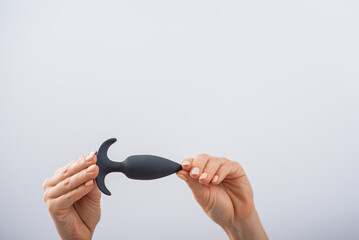 Faceless woman holding a black anal plug on a white background. Assortment of sex shop