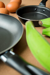 Black pan with oil, some eggs and green bananas on a table to be fried 