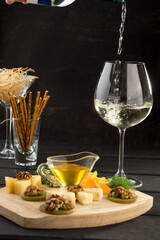 glass of white wine with Antipasto or catering cheese and walnut platter on black background