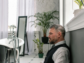 Fototapeta premium handsome mature courageous stylish scotsman businessman in kilt sitting on the floor in bathroom. Style, work from home, fashion, lifestyle, culture, ethnic concept.