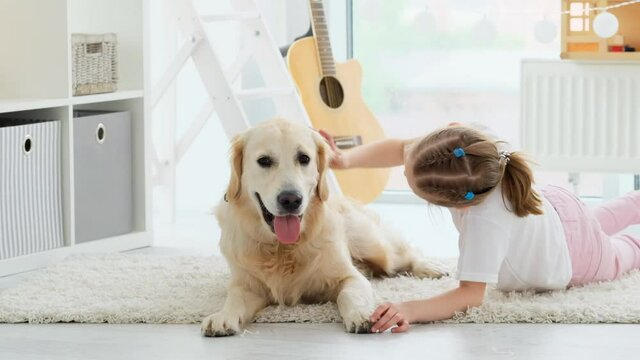 Cute golden retriever dog kissing little girl on floor in kids room