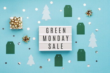 Green Monday sale text on white Lightbox with gold gift box and Christmas decorations on blue paper background.