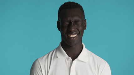 Attractive African American man in white T-shirt joyfully posing on camera over blue background. Happy expression