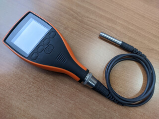 The device for measuring the thickness of the paint is on the table. Part of the image is out of focus.