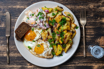 Ukrainian food, fried potatoes with onions, eggs, vegetable salad, black bread and glass of vodka on wooden background